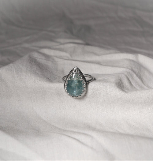 Teardrop-shaped blue gemstone ring on a white fabric surface